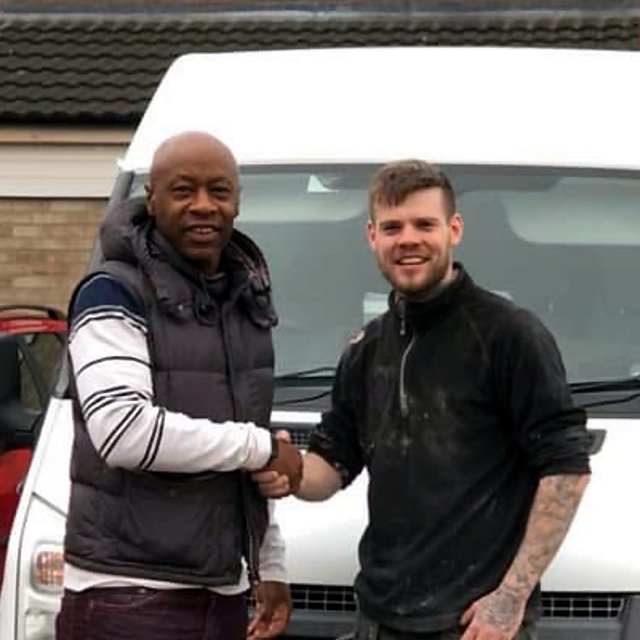 Tom, plaster still on his top, shaking a customer's hand in front of his van